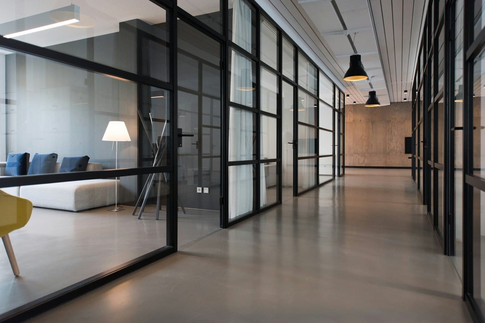 Glass-partitioned office corridor with meeting rooms along one side